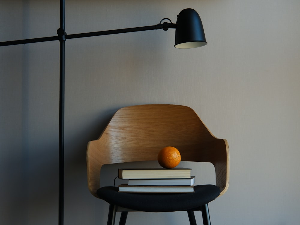 an orange sitting on top of a stack of books next to a lamp