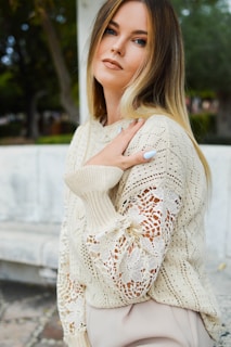A model wearing a cream-colored knitted sweater standing outdoors on a crisp autumn day.