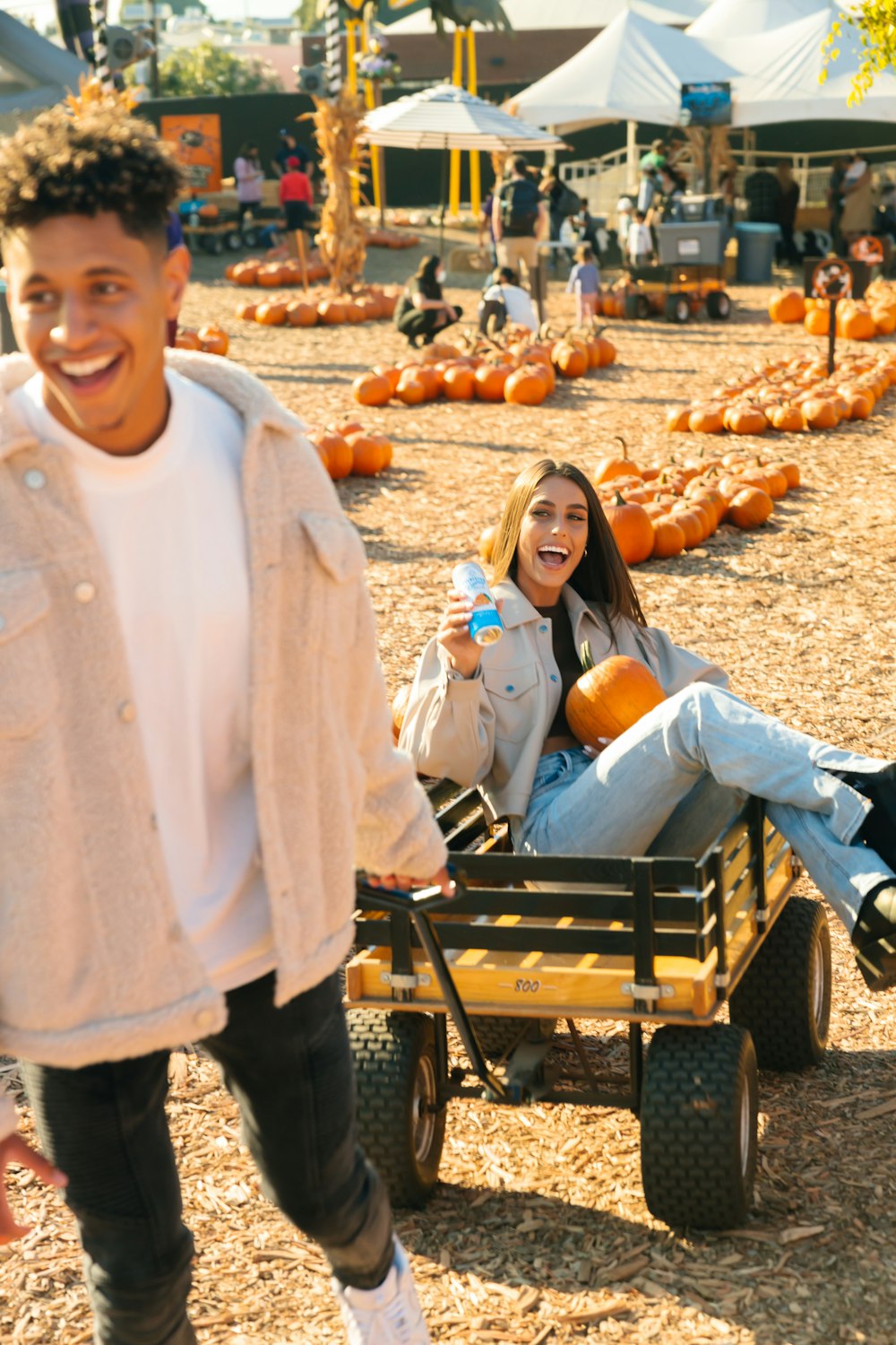 a man and a woman riding in a wagon with pumpkins