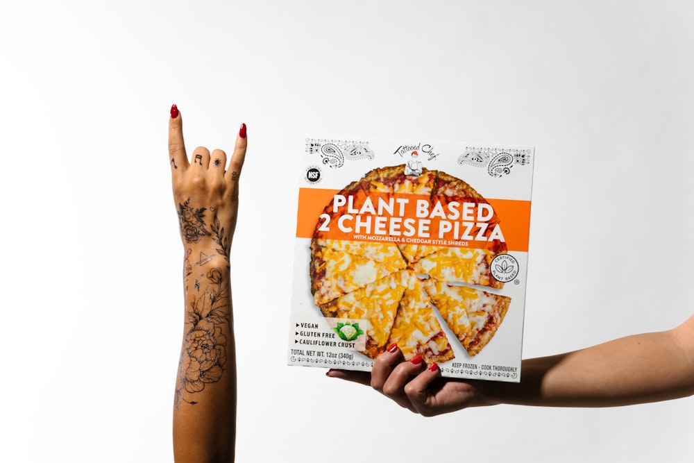 a hand holding a box of plant based cheese pizza