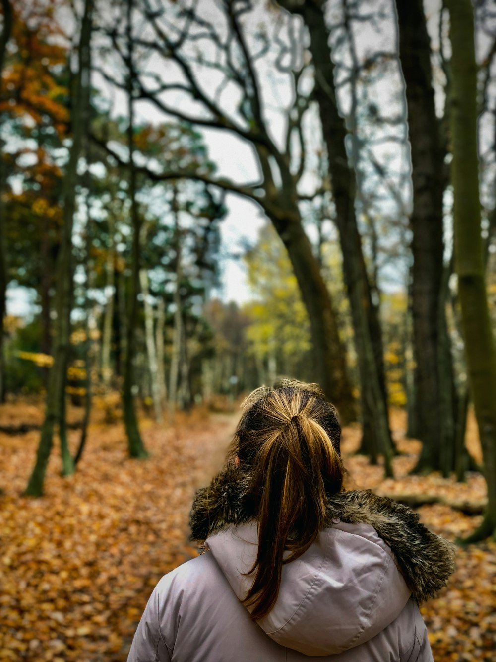 a woman in a white jacket walking through a forest