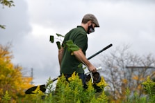 a man in a green shirt holding a pair of gardening tools