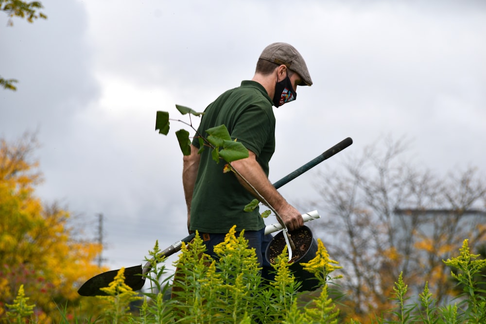 a man in a green shirt holding a pair of gardening tools