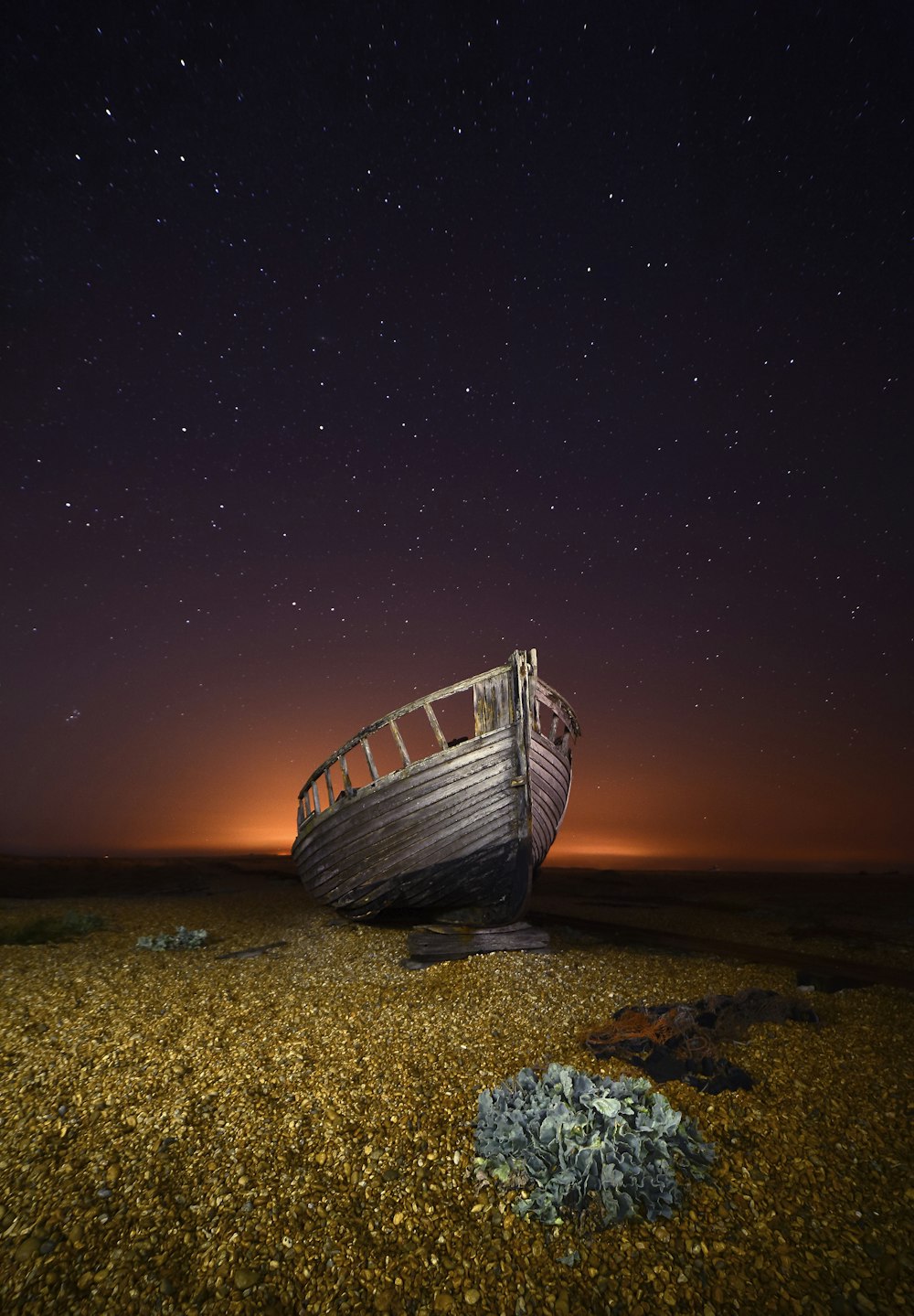 a boat sitting on top of a sandy beach under a night sky