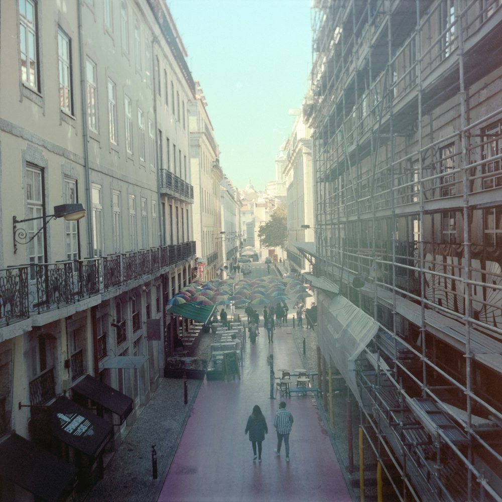 a couple of people walking down a street next to tall buildings