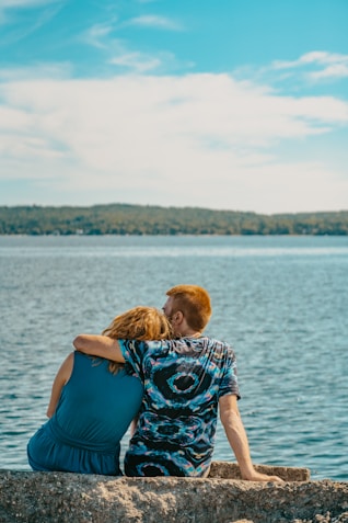 a man and a woman sitting on a rock by the water