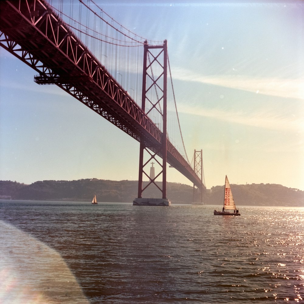 a sailboat sailing under a bridge on a sunny day