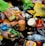 An assortment of discarded food packaging, including plastic bags, bottles, jars, and snack wrappers, strewn across a dark surface. Items such as a loaf of bread, jars labeled Tostitos, a plastic bottle of water, and various snack wrappers are visible.