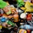 An assortment of discarded food packaging, including plastic bags, bottles, jars, and snack wrappers, strewn across a dark surface. Items such as a loaf of bread, jars labeled Tostitos, a plastic bottle of water, and various snack wrappers are visible.