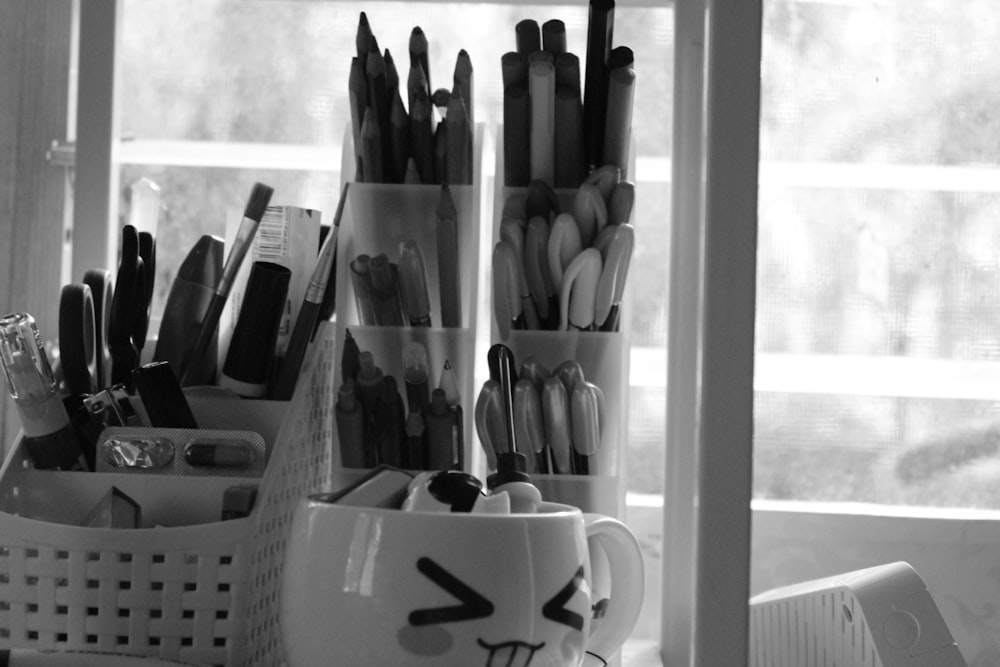 a cup filled with pens and pencils next to a window