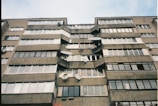 A multi-story residential building with numerous windows and satellite dishes attached to the exterior. The structure is made of concrete and brick, exhibiting a utilitarian architectural style.
