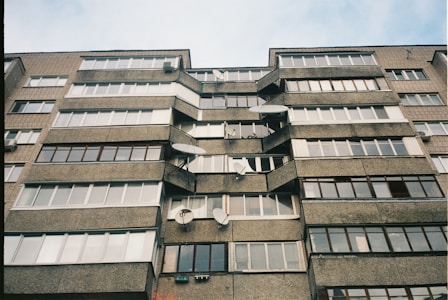 A multi-story residential building with numerous windows and satellite dishes attached to the exterior. The structure is made of concrete and brick, exhibiting a utilitarian architectural style.