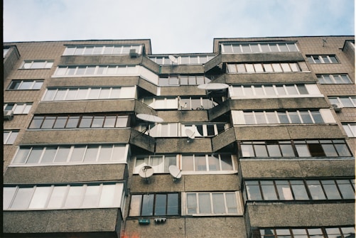 A multi-story residential building with numerous windows and satellite dishes attached to the exterior. The structure is made of concrete and brick, exhibiting a utilitarian architectural style.