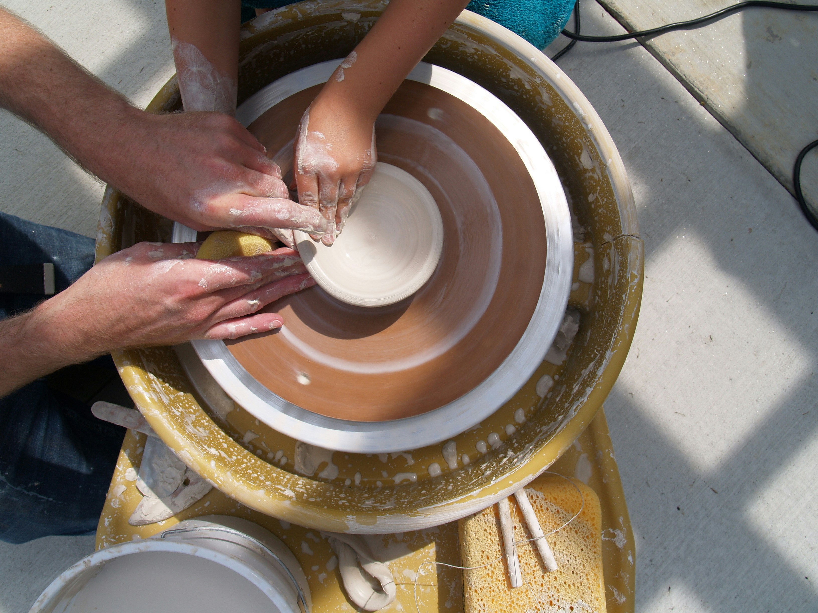 Adult helping a child learn to throw on the potter's wheel.