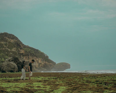 A candid moment of a couple walking hand in hand along a charcoal-colored rocky shoreline.