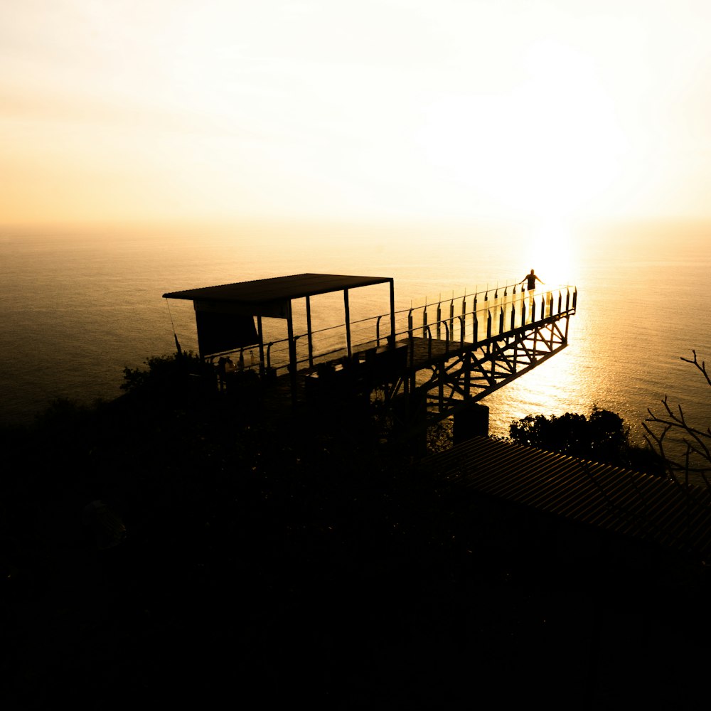 the sun is setting over the water and a small structure on a hill