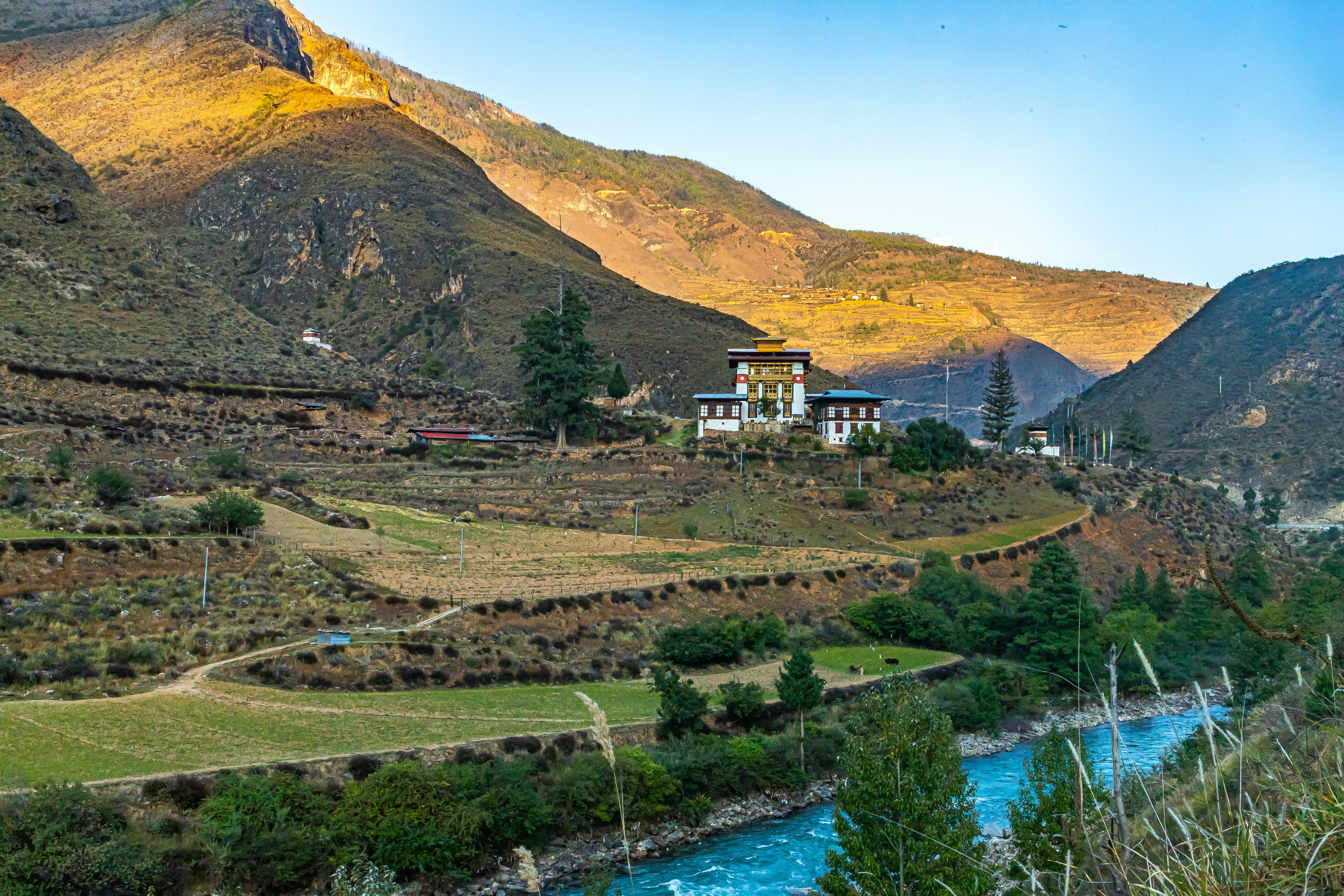 a house in the middle of a valley surrounded by mountains, Located about 30 minutes drive from Paro to Thimphu, the temple built by the famous 13th century bridge builder Buddhist saint Thangthong Gyalpo sits across the Pachhu (Paro River).