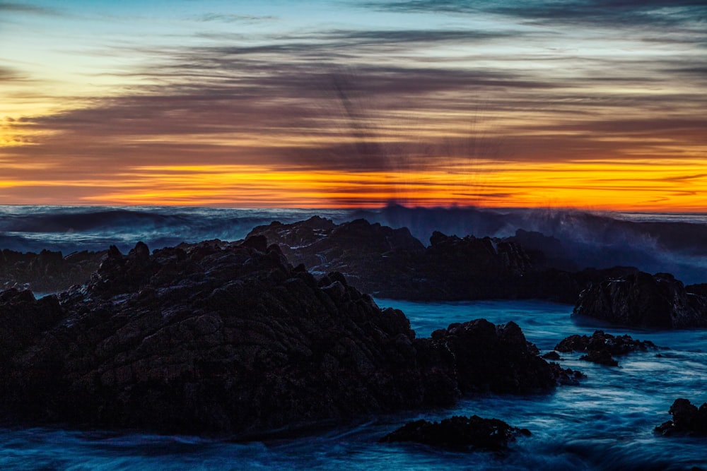 the sun is setting over the ocean and rocks