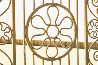 Ornate metal gate with circular flower patterns, crafted from pale yellow metal bars against a soft, blurred background.