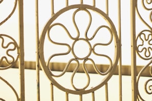 Ornate metal gate with circular flower patterns, crafted from pale yellow metal bars against a soft, blurred background.
