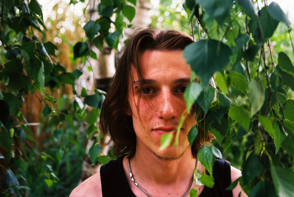 a man standing in front of a bunch of green leaves