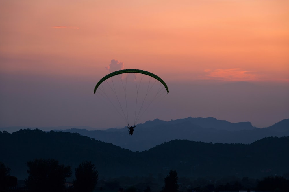a paraglider flying over a mountain range at sunset