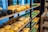 A store shelf displays a variety of cheese wheels in different colors and sizes, organized neatly on wooden shelves. The cheeses range from black and yellow to green, indicating various types and flavors. Small blackboards with labels and prices are placed in front of some cheeses. On an adjacent shelf, there are cheese packages shaped like wedges.