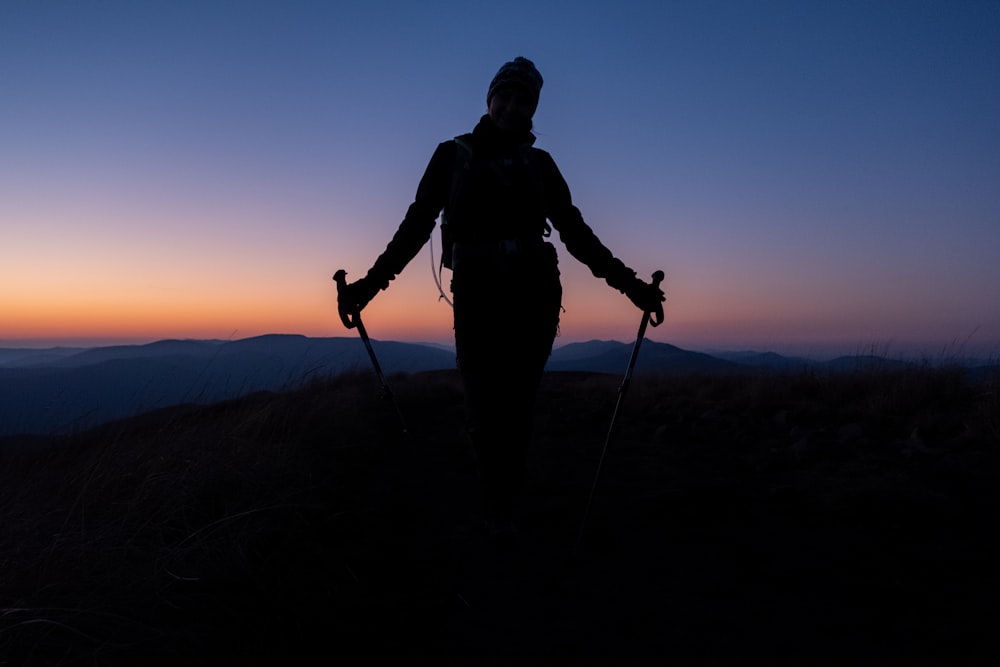 uma pessoa em pé no topo de uma colina segurando bastões de esqui