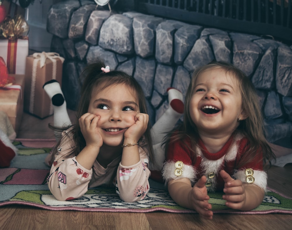 two little girls laying on the floor next to a christmas tree