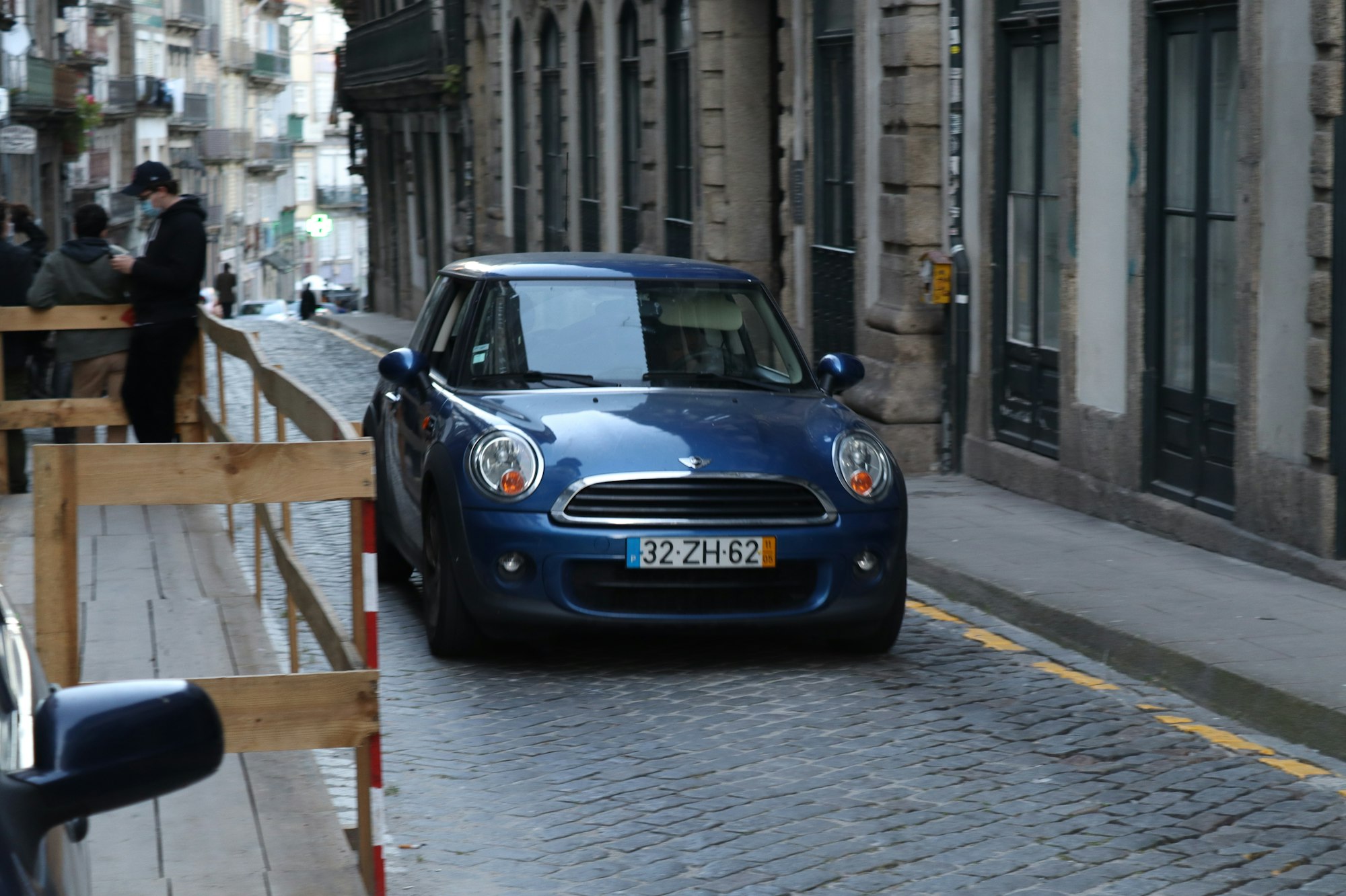 a small blue car driving down a street next to tall buildings
