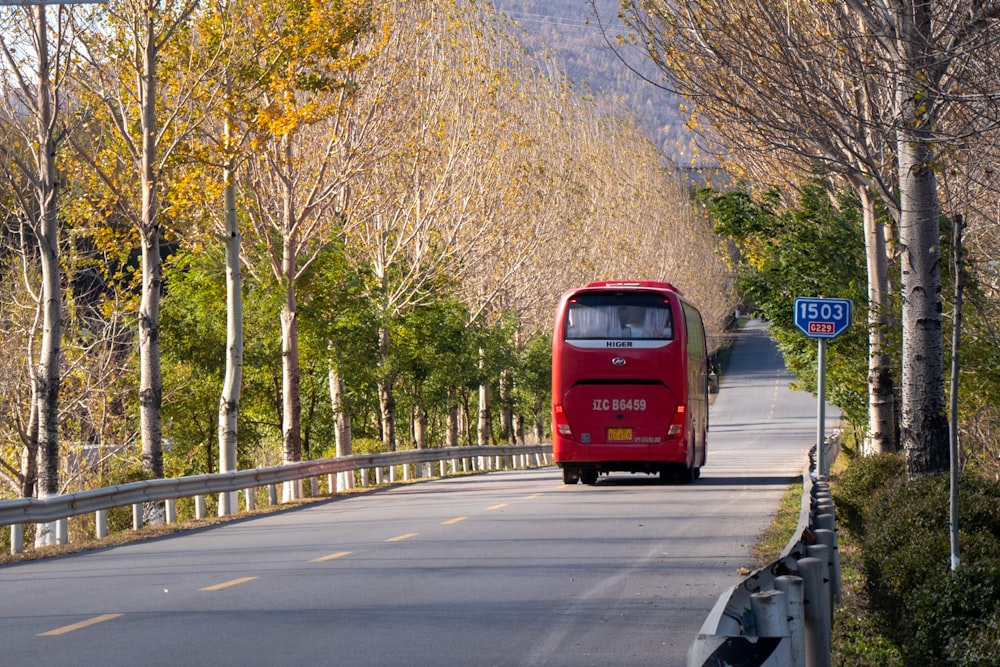 a red bus driving down a street next to a forest