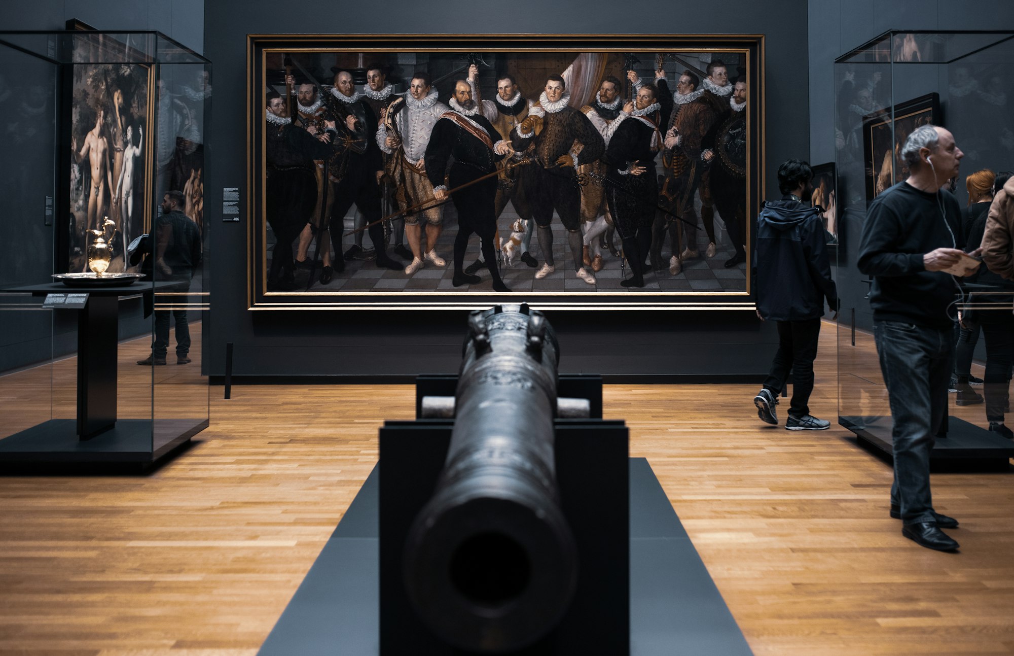 a museum gallery with an antique cannon perpendicular to a painting of men in baroque dress