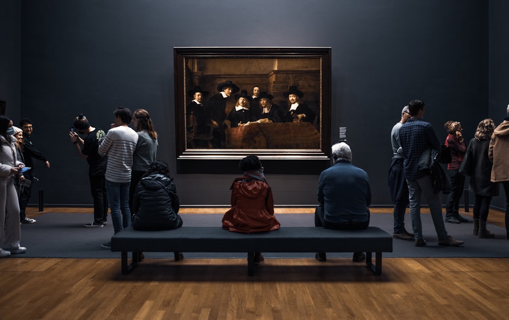 a group of people standing around a museum looking at a painting