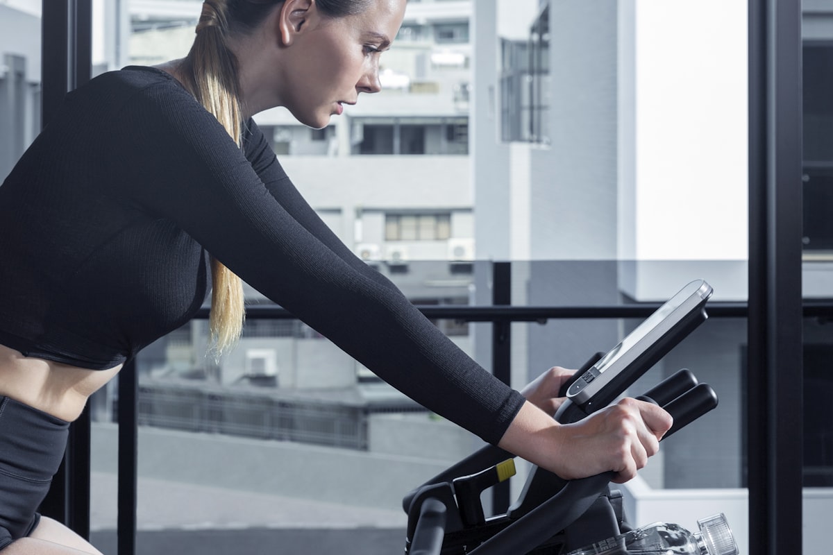A woman on a stationary exercise bike with a digital tablet screen