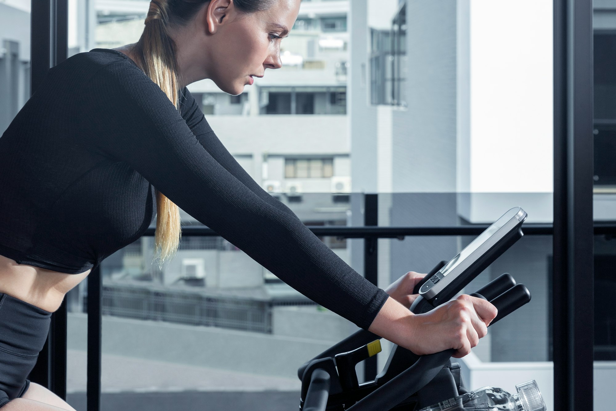 Young fit woman, gazes down at the bike console whilst exercising at home on an Intenza 550 GC3 Group Cycle.