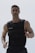 A muscular man is seen wearing a weighted vest, possibly for exercise or training. He has short hair and facial stubble, and appears focused and determined.