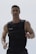 A muscular man is seen wearing a weighted vest, possibly for exercise or training. He has short hair and facial stubble, and appears focused and determined.