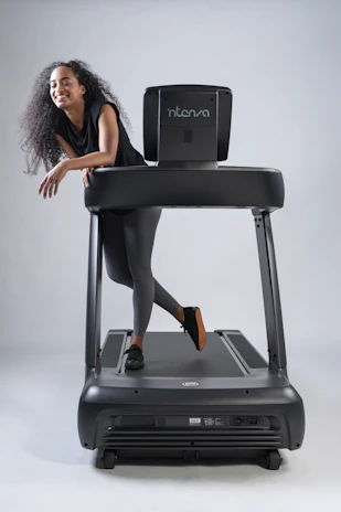 Smiling technician in branded Elektrovita uniform performing electrical maintenance on treadmill equipment.