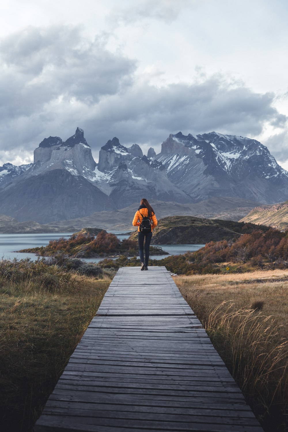 a person walking down a wooden walkway towards mountains