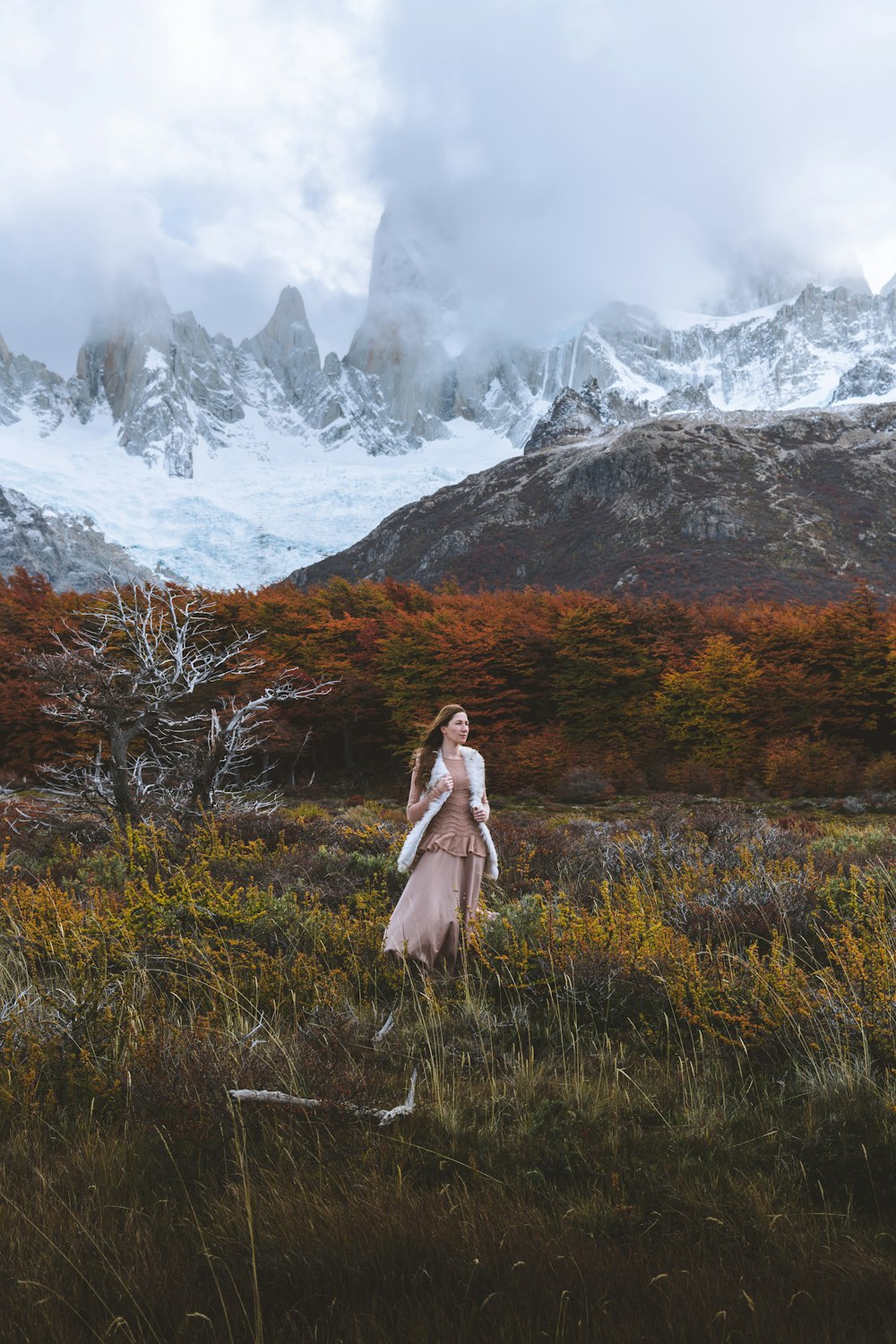 a woman standing in a field with mountains in the background