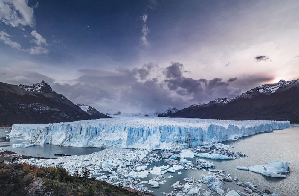 a large iceberg in the middle of a lake surrounded by mountains