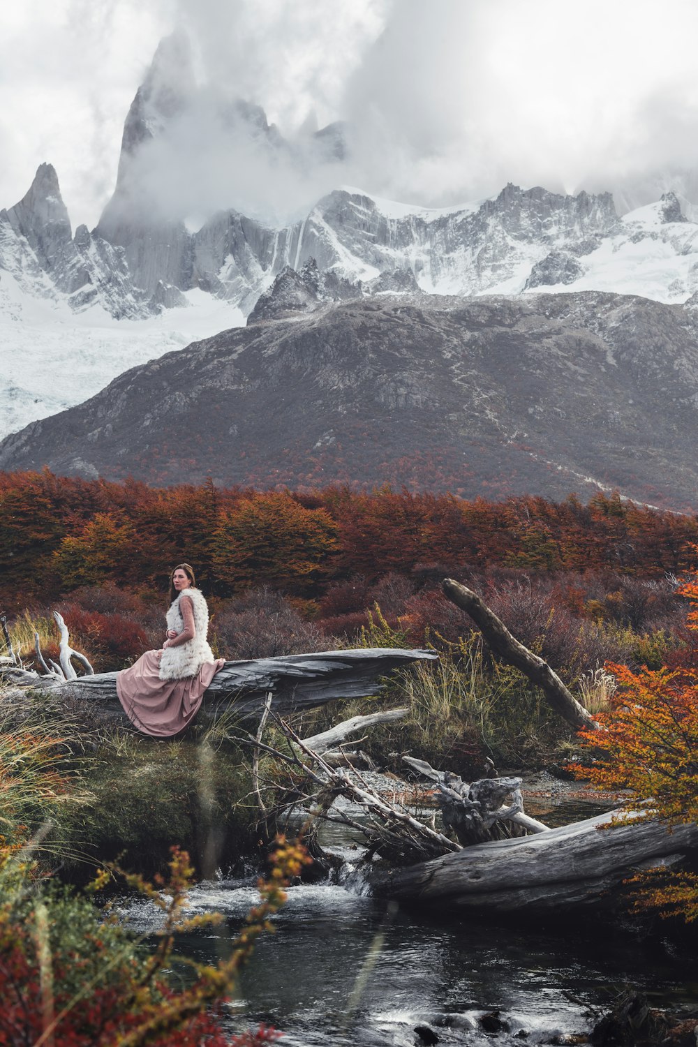 a woman in a long dress sitting on a log