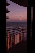 A spacious hotel balcony with a stunning view of the ocean at sunset.