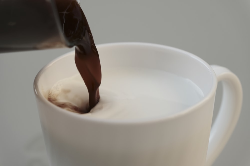 a person pouring chocolate into a white cup