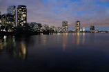 Black and white photo of city skyline reflected in calm water at dusk.