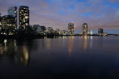 Black and white photo of city skyline reflected in calm water at dusk.