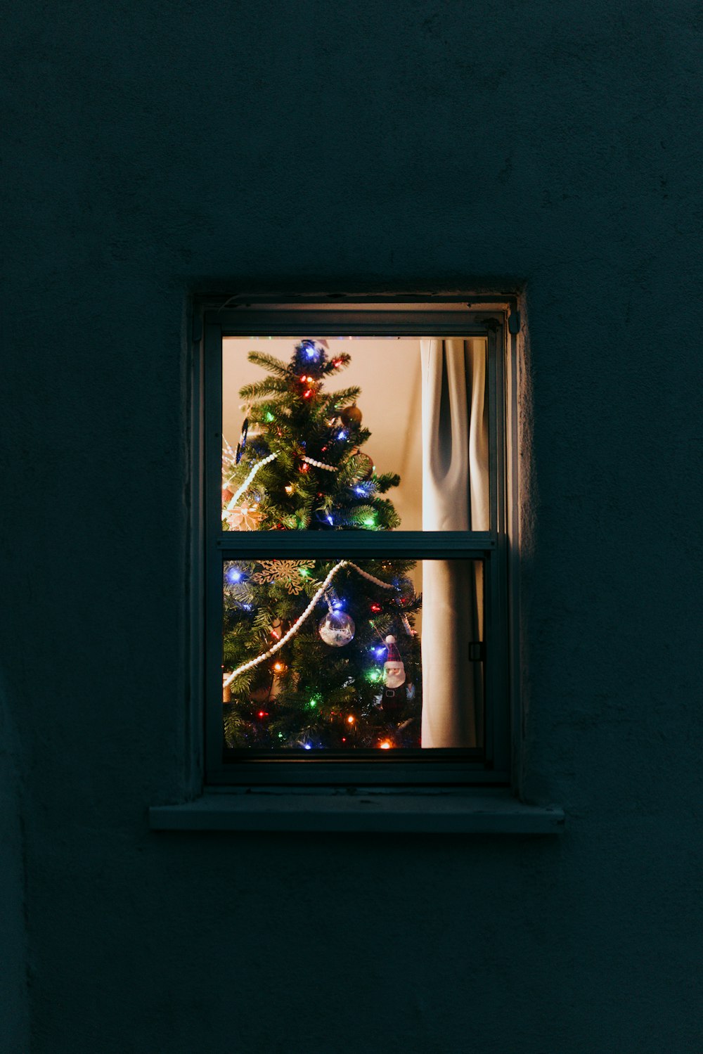 uma árvore de Natal é vista através de uma janela
