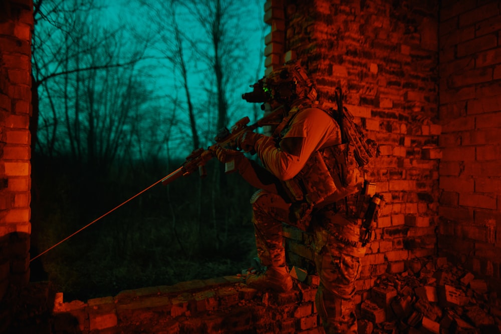 a man with a rifle standing on a brick wall
