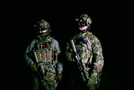 A high-definition photo of a team of elite operators in tactical gear surveying a guarded industrial perimeter at dusk.