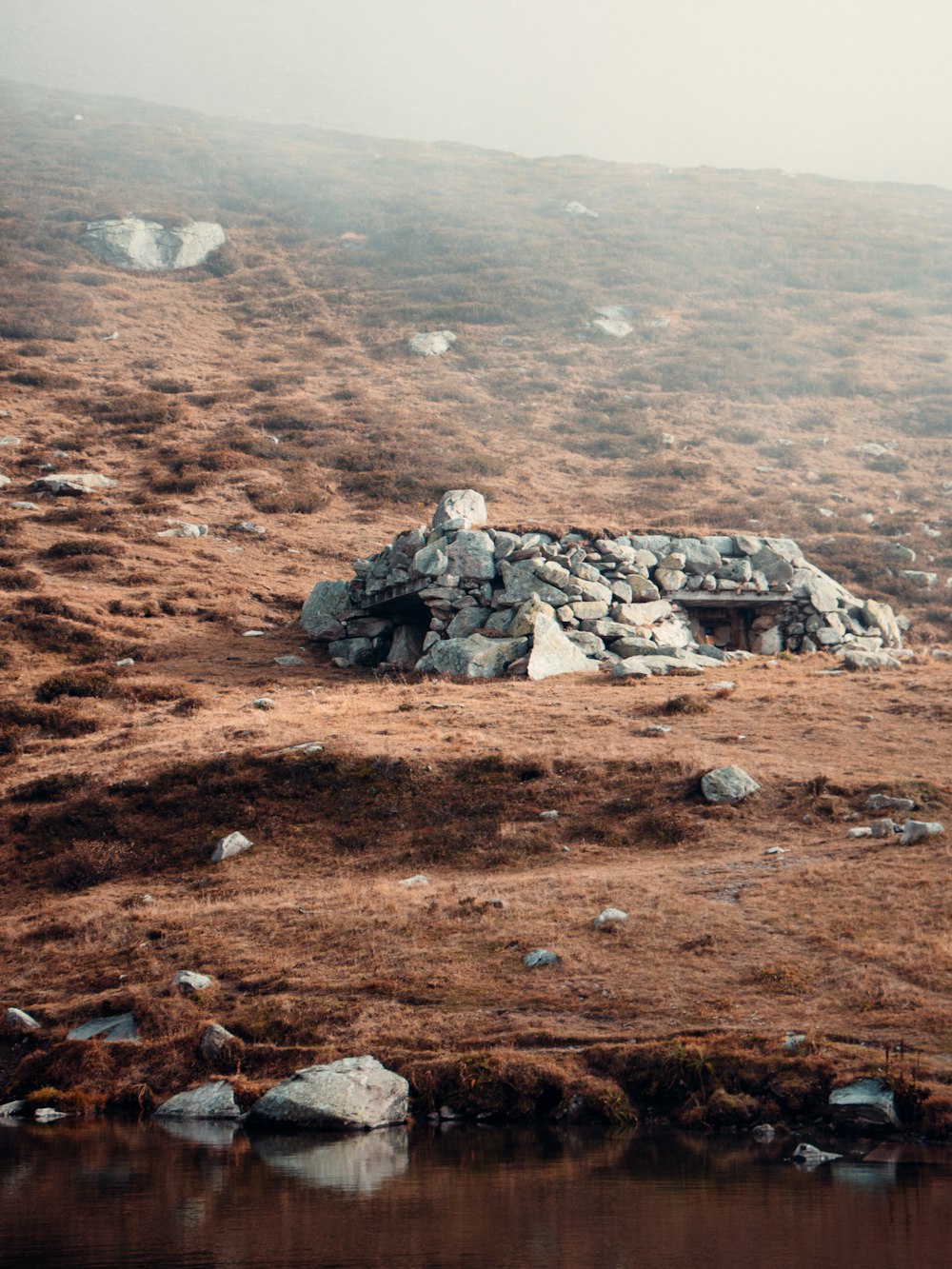 a stone hut on a hill with a body of water in the foreground